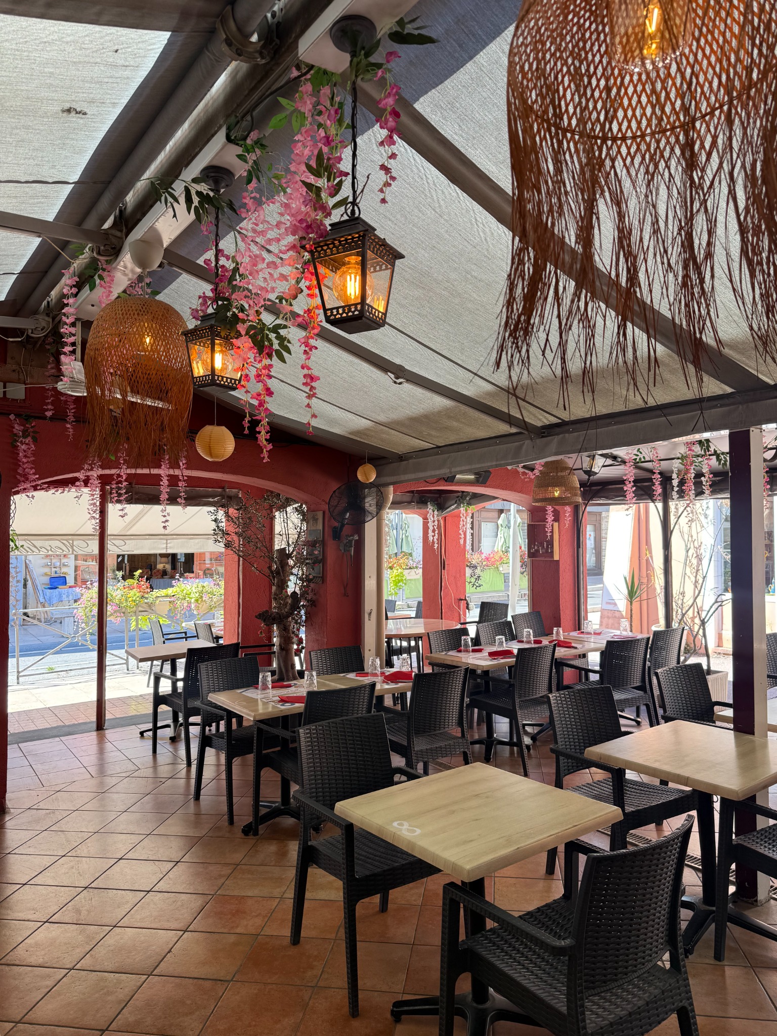 La terrasse couverte du Mesclun, ses tables dressées, ses lanternes et ses guirlandes de fleurs roses